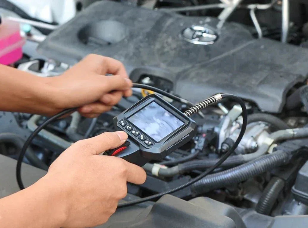 Hands using a handheld borescope inspection camera to examine a car engine